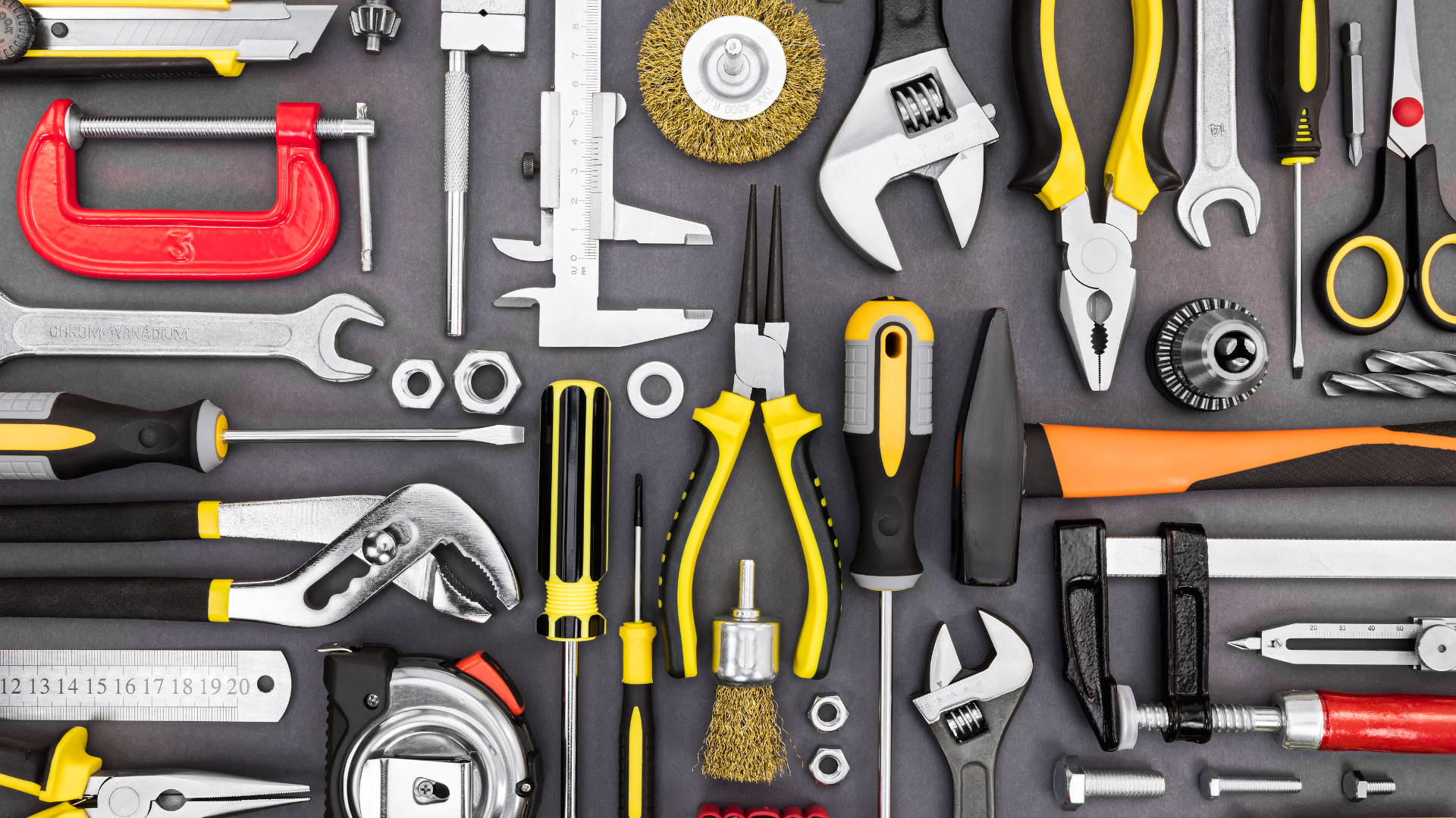 Hand tools, nuts, washers, and hardware arranged on a dark work surface.