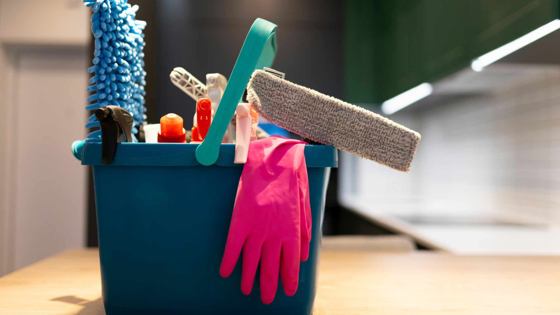 Blue bucket with cleaning supplies, including gloves, cloths, and sponges, indoors.