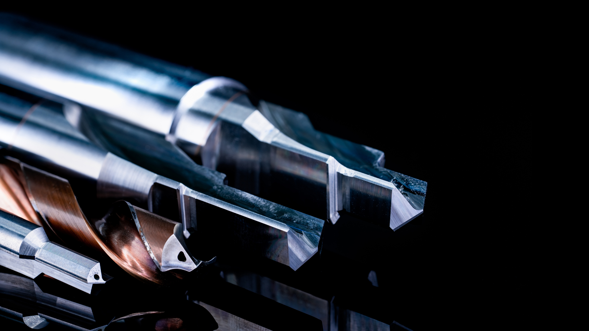Close-up of several metal drill bits with sharp cutting edges against a black background.