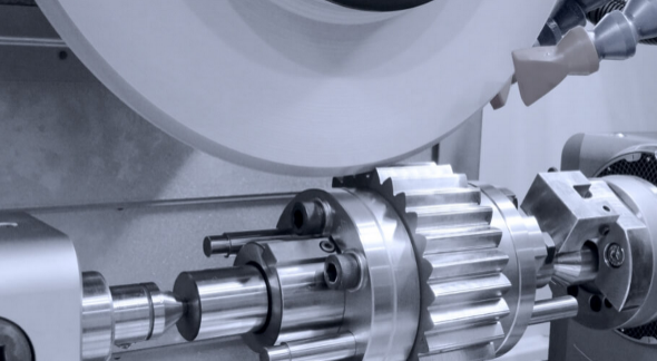 A gear grinding machine precisely shaping a metal gear with a rotating abrasive wheel.