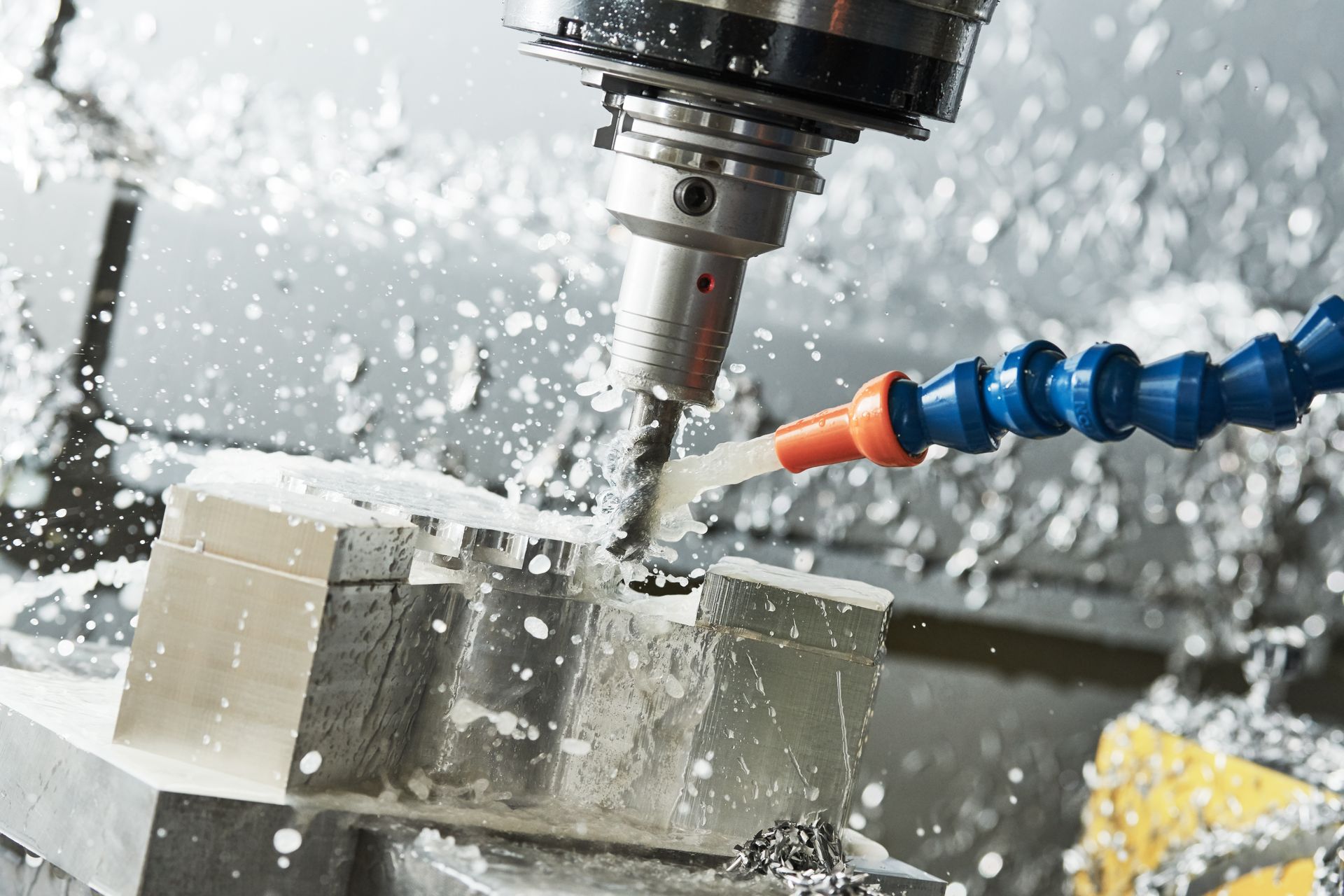 CNC machine cutting metal block with coolant spraying.